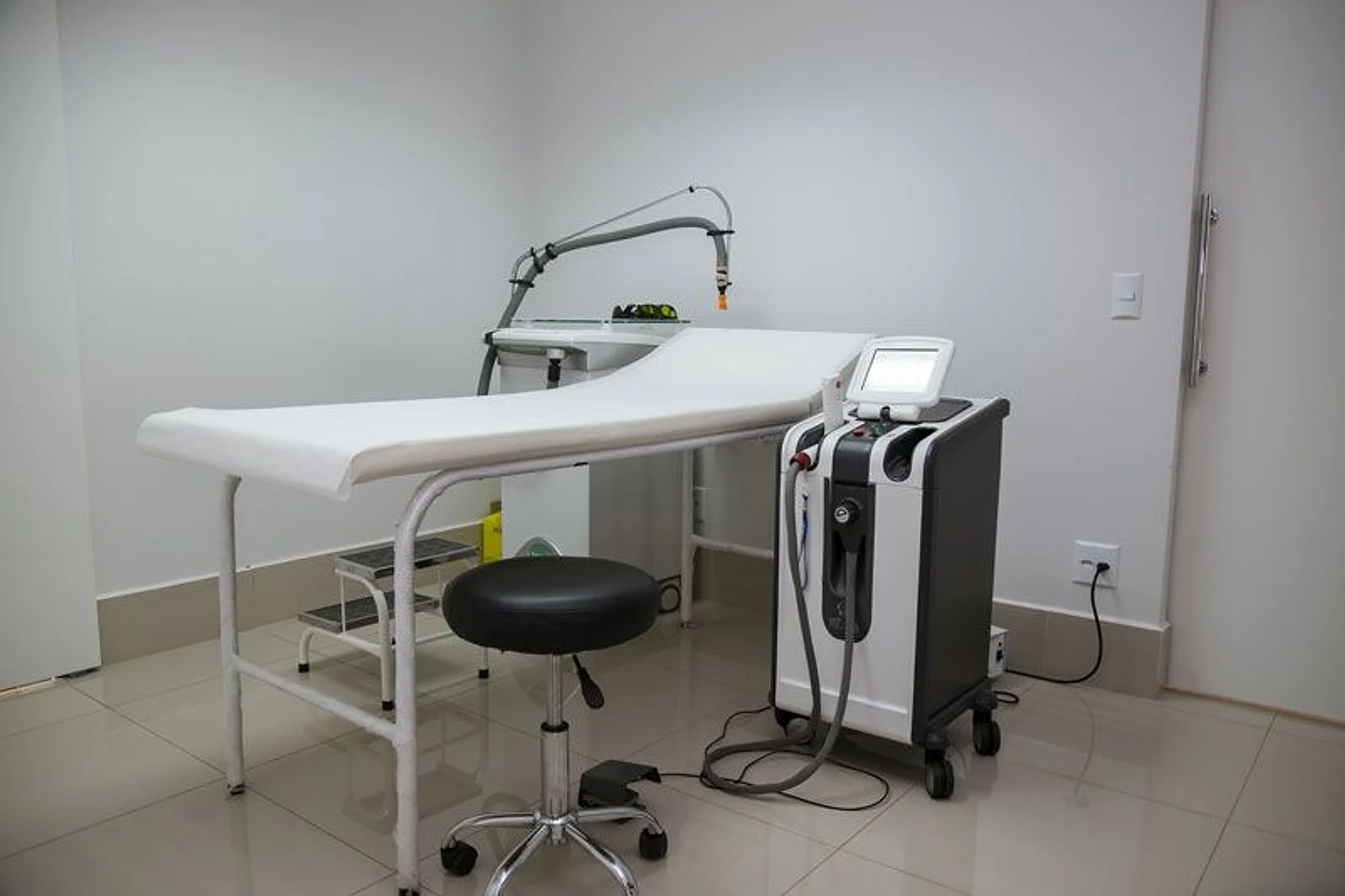 Sala de laser do consultório: maca branca, banqueta preta e o aparelho de laser ao lado